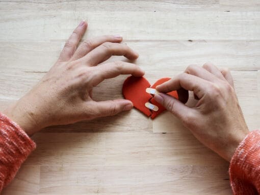 Hands bandaging a broken paper heart